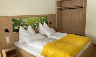 A cozy bedroom with a double bed and white pillows. The yellow blanket and the wooden structure create an inviting atmosphere.
