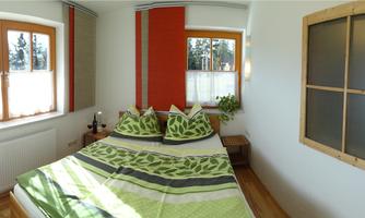 A cozy bedroom with a double bed and colorful cushions. Large windows provide plenty of light and an inviting atmosphere.