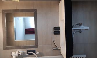 A modern bathroom with a large mirror above a white sink. In the background, red curtains and a light wall paneling are visible.