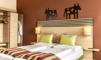 A modern hotel room with a double bed and colorful pillows. Decorative cow silhouettes hang on the wall.