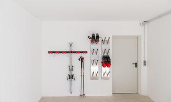 A clean garage space with a ski rack and skis. Ski boots and poles are hanging on the wall in an orderly fashion.
