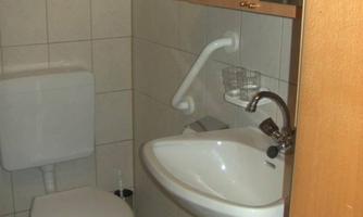 A small bathroom with a toilet and a sink. Towels hang on the wall and a mirror is visible.