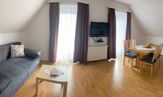 A bright living room with a comfortable sofa, a table, and chairs. Large windows provide plenty of daylight.
