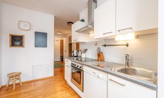 A modern kitchen with bright furniture and wooden flooring. The kitchen equipment is functional and well-organized.