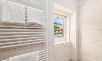A modern bathroom with a white towel heater and fresh towels. The view of the landscape is visible through the window.