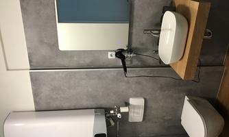A modern bathroom with a white sink and a mirror. The walls are in a gray shade and there is a toilet installation.