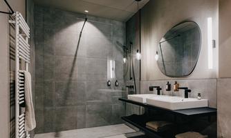 A modern bathroom with gray tiles and a large shower. There is an elegant sink with a black under-cabinet.