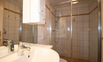 A modern bathroom with a shower and a sink. The walls are tiled in light colors and there is a large mirror.