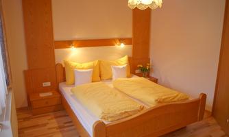A cozy bedroom with a double bed and yellow pillows. The wooden furniture and soft lighting create a friendly atmosphere.