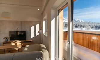 A bright living room with a television and a cozy sofa. Through the windows, a snowy mountain landscape can be seen.