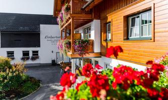 A charming wooden house with colorful balcony flowers. In the background, a light facade and a clear sky can be seen.