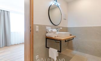 A modern bathroom with a stylish mirror and a wooden washbasin. Fresh towels are ready, and the space is bright and inviting.