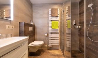 A modern bathroom with shower and toilet. The walls are in neutral tones and there are towels in vibrant colors.