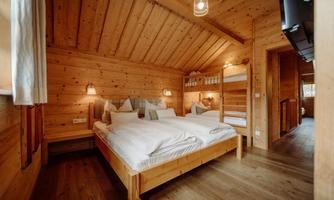 A cozy wooden bedroom with two single beds and a bunk bed. The warm tones and indirect lighting create an inviting atmosphere.