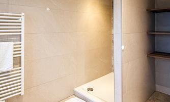 A modern bathroom with a shower niche and a towel holder. The floor is made of light stone, and the walls are in neutral colors.