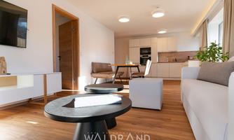 A modern living room with a cozy sofa and a dining table. The large windows let in plenty of light and create an inviting atmosphere.