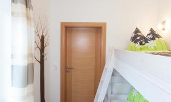 A small room with a bunk bed and colorful cushions. The walls are light and the decor feels modern and welcoming.