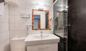 A modern bathroom with white tiles and a large mirror. There is a glass shower and a sink with an elegant design.