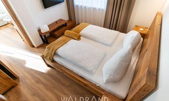 A cozy bedroom with a wooden bed and two large pillows. The warm tones and the daylight create an inviting atmosphere.