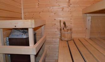 A cozy sauna room with wooden paneling. On the right, the loungers and a bucket for water can be seen.