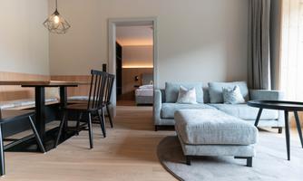 A modern apartment with a cozy sofa and a dining table. Large windows provide lots of light and create an inviting space.