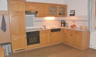 A cozy kitchen with wooden furniture and modern appliances. The walls are decorated with white tiles and mosaics.