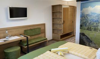 A modern room with two beds, a TV, and a wardrobe.  
On the wall, there is a mountain motif, and there is a cozy seating area.