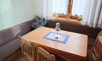 An inviting dining area with a wooden table and four chairs. The windows are bright and adorned with curtains, and there is a cozy corner bench.