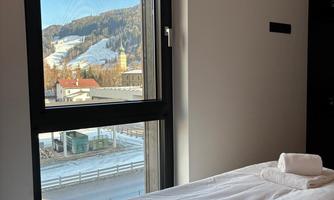 A modern room with a bed and fresh towels. A scenic mountain landscape can be seen through the window.