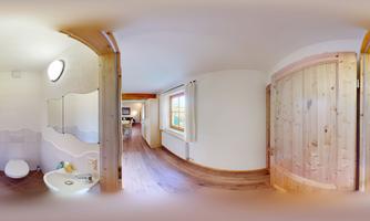 A modern bathroom with light wood and a large mirror. There is a door that leads to another room.