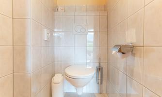 A modern bathroom with white tiles and a clean toilet. There is a paper holder and a trash can.