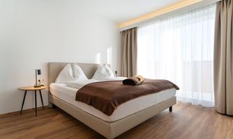 A modern bedroom with a large bed and bright curtains. The floor is made of wood and creates a cozy atmosphere.