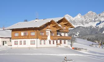 A cozy chalet in the snow, surrounded by impressive mountains. The clear blue sky offers a perfect winter landscape.