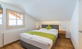 A modern bedroom with a cozy bed and a green pillow. Bright walls and plenty of daylight create an inviting atmosphere.