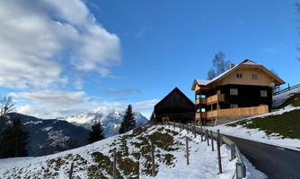 A picturesque winter village with snow-covered hills. In the background, there are mountains and a blue sky.