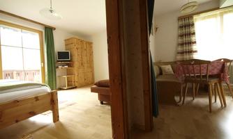 A cozy room with wooden details and a single bed. There is a dining area with a table and chairs, as well as a window with a view outside.