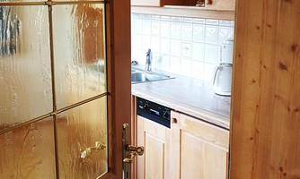 A look into a well-equipped kitchen with wooden cabinets and a countertop. The glass door provides plenty of light in the room.