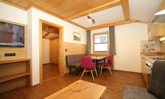 A cozy living area with wooden walls and a dining table. The modern kitchen is well-equipped and the windows provide plenty of natural light.