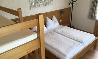 A simple room with a double bed and a bunk bed. The walls are bright and the furniture is made of wood.