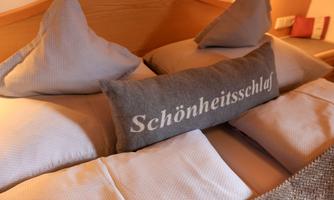 A comfortable bed with two pillows and a decorative pillow. The pillow has the text "Beauty Sleep" on it.