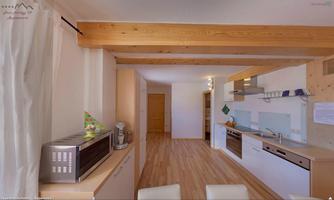 A modern kitchen with a wooden ceiling and light-colored furniture. The room is designed to be bright and welcoming.