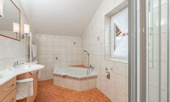 A modern bathroom with a bathtub and an elegant sink. The walls are light tiled, and a window provides natural light.