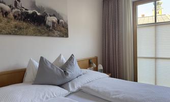 A cozy bedroom with two single beds and soft pillows. A window provides natural light and offers a view outside.