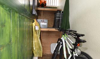 A narrow hallway with wooden floors and green walls. In the foreground are two bicycles, and in the background are various objects visible.