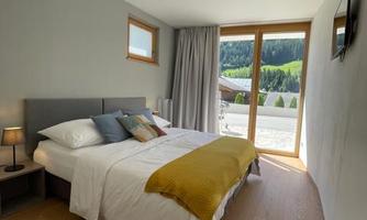 A modern bedroom with a double bed and colorful pillows. Large windows offer a view of nature.