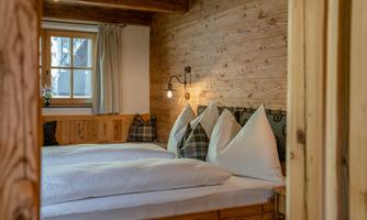 A cozy bedroom with wooden ceilings and two beds. The bedding is white, and there are decorative pillows in the background.
