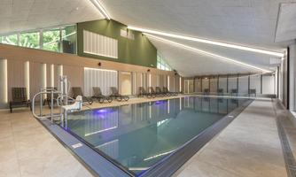 A modern indoor pool with bright water and elegant loungers. Large windows allow plenty of natural light inside.