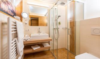 A modern bathroom with a glass shower and a sink. The walls are bright, and there are wooden details for a warm look.
