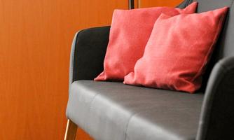 A modern black armchair with red cushions is positioned in front of a door. The floor is made of wood, adding a warm atmosphere to the room.