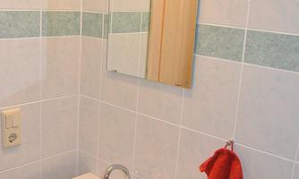 A small bathroom with a white sink and a mirror. A red towel hangs on a hook next to the sink.
